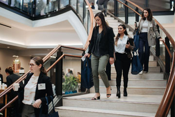 four female students in business casual walk down the stairs at Caruso law school