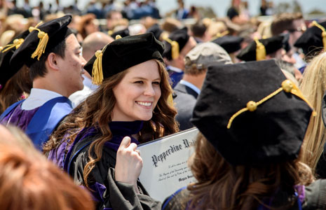 A female student proudly holds her Pepperdine diploma at graduation