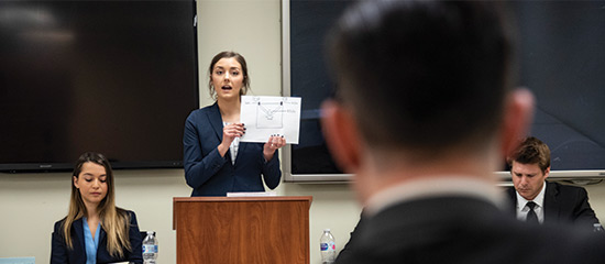 a female student presents her case holding a piece of paper up at a moot court competition 