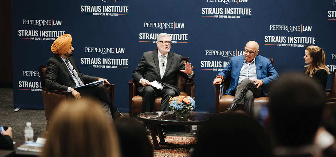 Four people sit and talk on a stage at a Staus Institute event