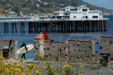 a surfer walks down to Surfrider beach by the Malibu Pier