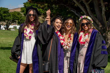 four females celebrating wearing graduation robes and caps and leis