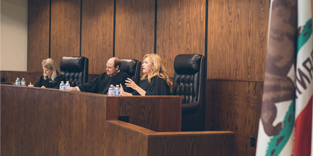 Three judges sitting at the bench with the California state flag