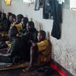 inmates sit along a wall in a Ugandan prison
