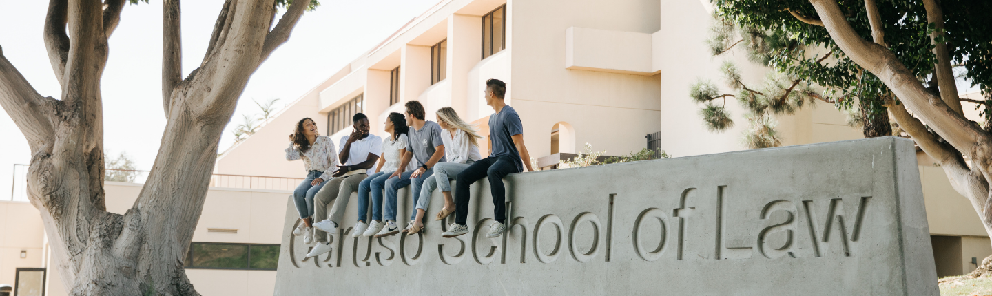six students sit atop the Caruso School of Law monument sign