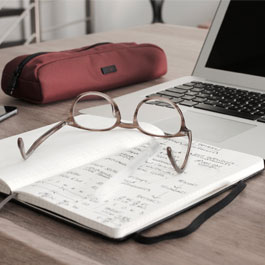 glasses set on top of a notebook next to a laptop