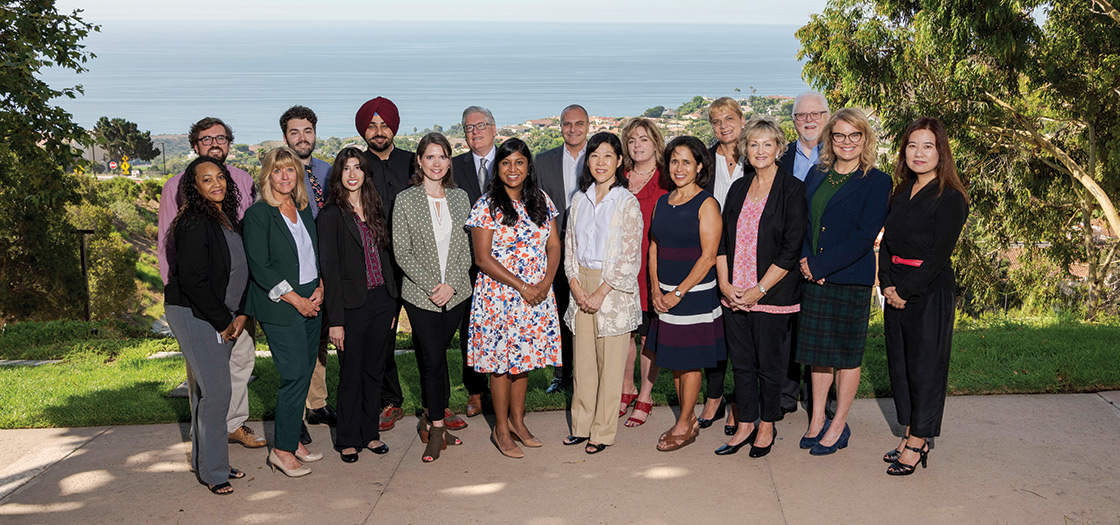 The entire Straus staff standing outside for a group photo with the Pacific ocean visible in the background