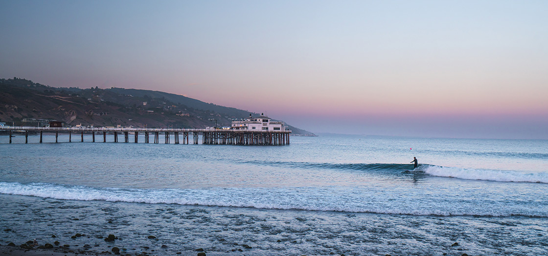  surfer riding a wave at dusk in front of the  famed Malibu pier