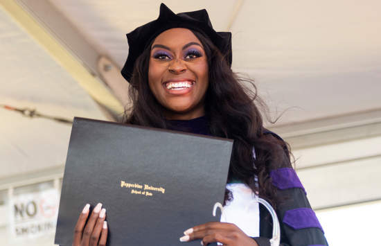 A graduate smiles holding her diploma