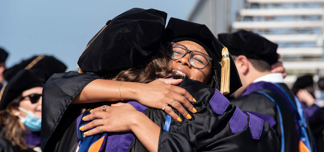 Two graduates embraced in a hug at commencement for the Class of 2020
