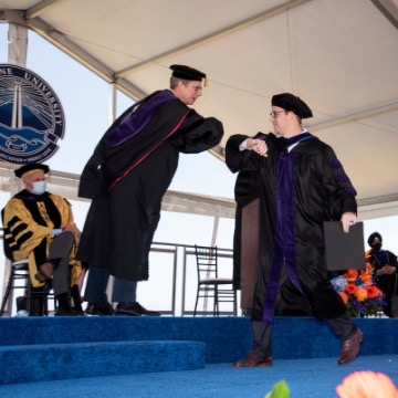 Photo of 2021 graduate with Dean Caron on commencement stage