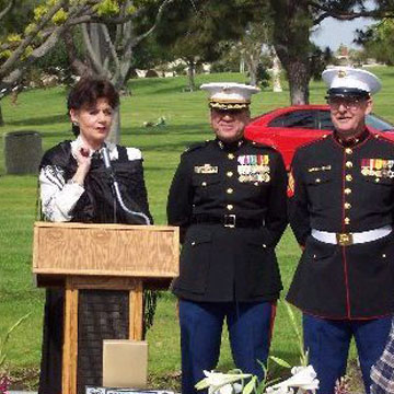 Eileen Moore speaking at a podium with two veterans in uniform two her left