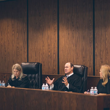 two female judges sit on either side of a male judge on the bench