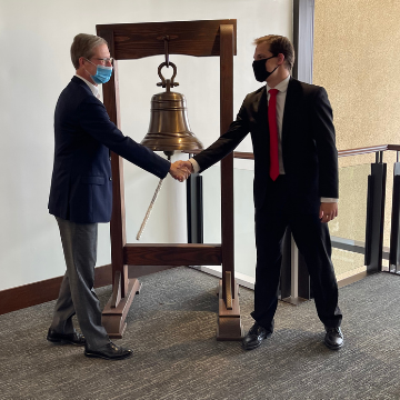 Seth Shepherd shakes the hand of the dean in front of the bell